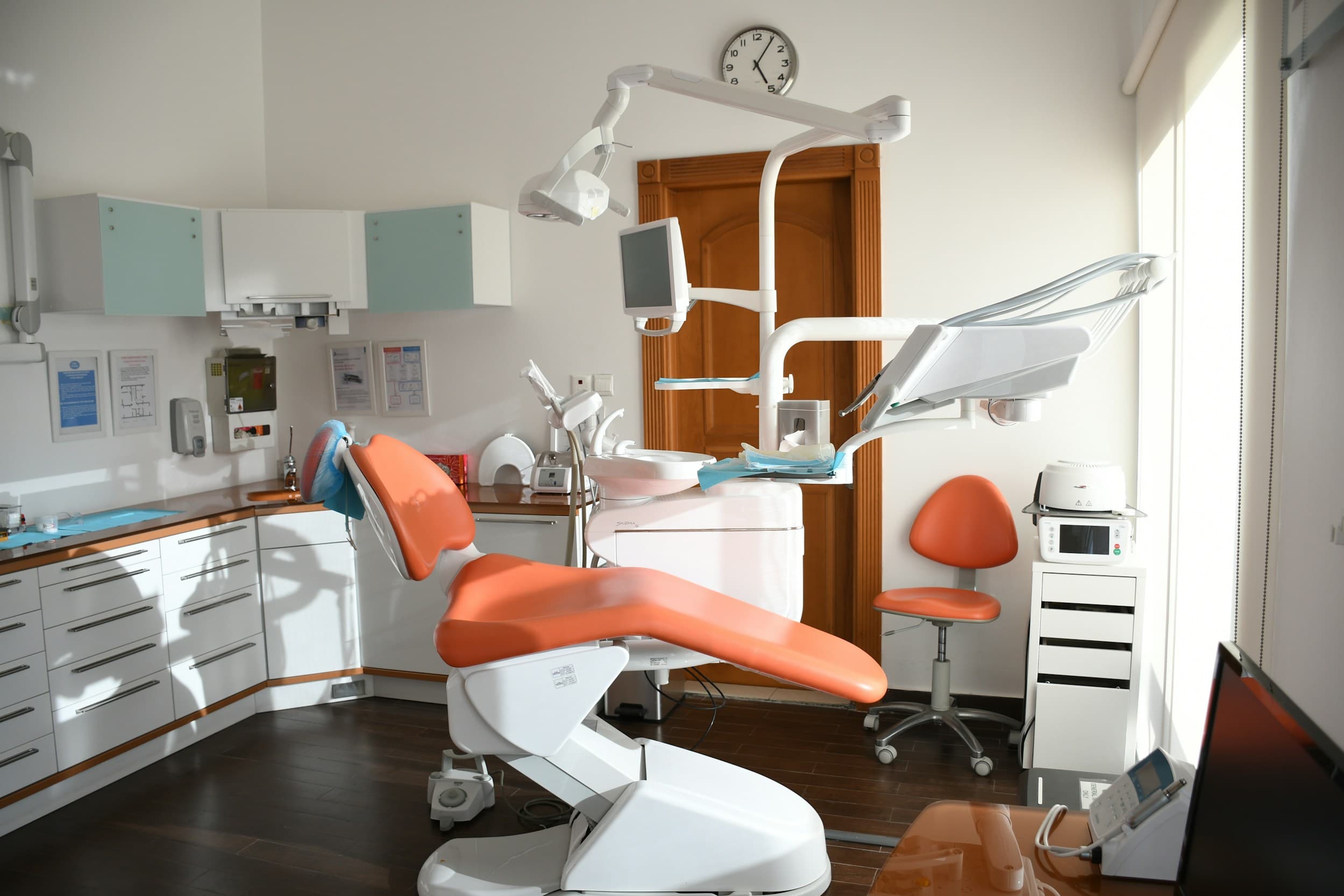 A bright dental surgery with an orange treatment chair and warm wood cabinetry